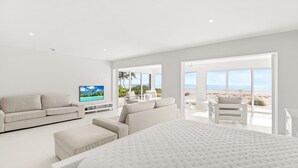 A modern bedroom with a large bed, a sofa, a TV, and a balcony with a beach view. - Gulf Front Condo! Modern Updated Condo on the Sand ! (Sanibel)