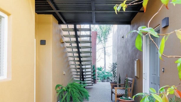 A covered outdoor area with a wooden bench, potted plants, and a staircase leading to a balcony. -  Downtown Napa!  Unit B Walk to Everything! (Napa)