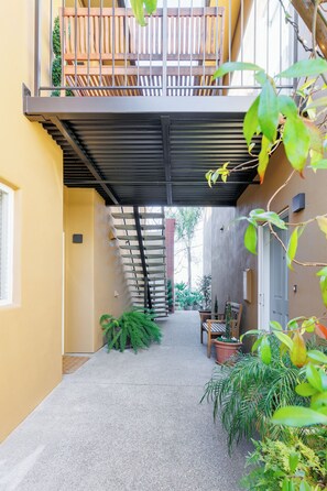 A covered outdoor area with a wooden bench, potted plants, and a staircase leading to a balcony. - Downtown Napa! Unit B Walk to Everything! (Napa)