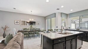 Una cocina moderna con una isla central, muebles oscuros y un comedor con candelabro.