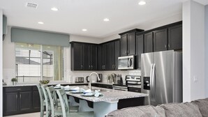 Una cocina moderna con armarios oscuros, electrodomésticos de acero inoxidable y una isla central con taburetes de bar.
