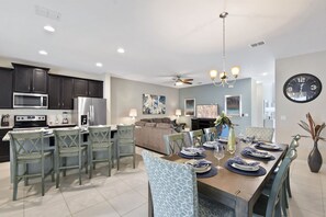 A modern kitchen with dark cabinets, a microwave, and a refrigerator. There is a dining area with a table set for four, chairs, and a chandelier.