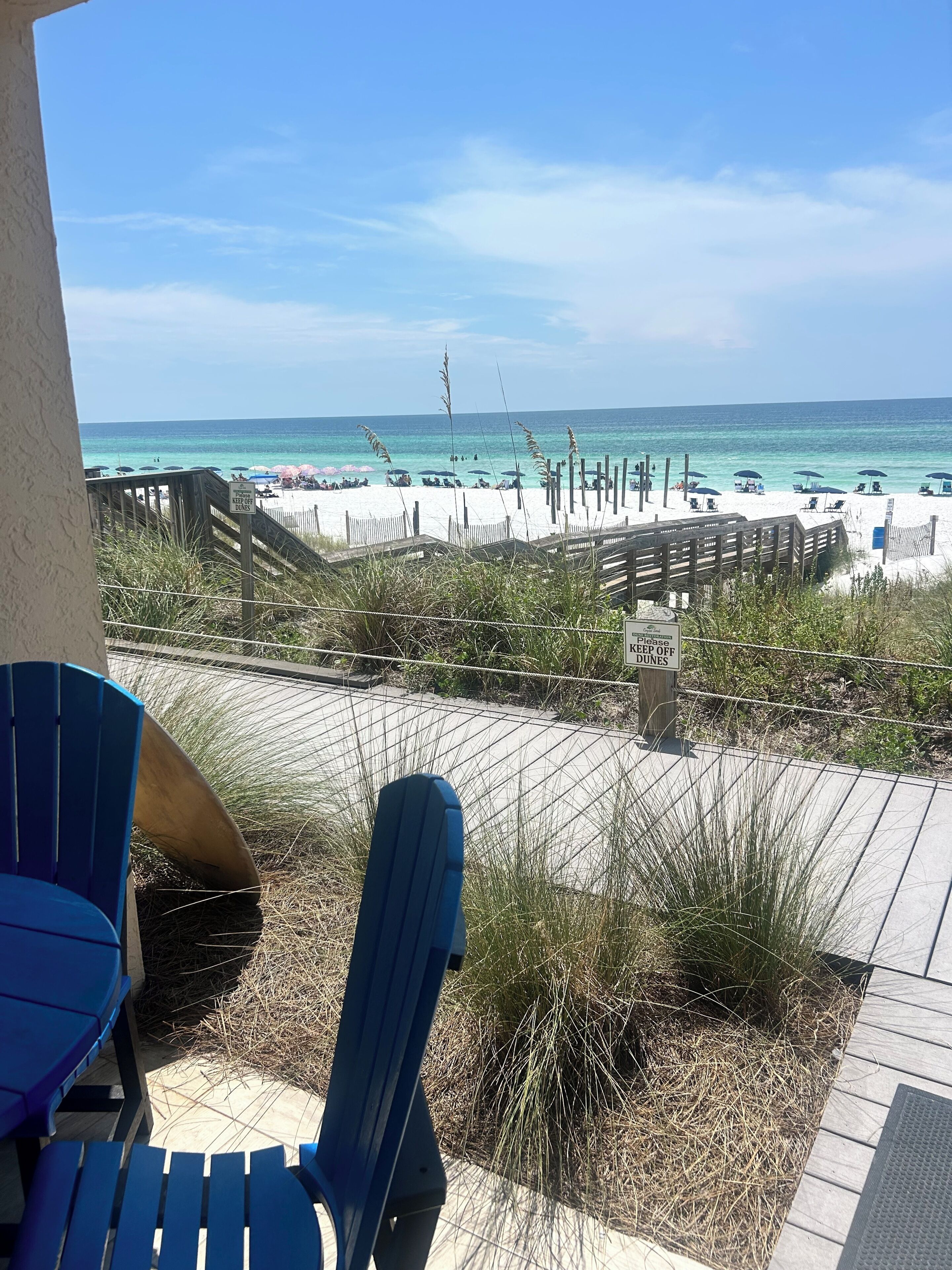 Vista de la playa con una terraza de madera, sillas y un letrero que advierte no pisar las dunas.