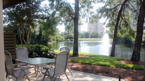 An outdoor patio with a glass table and chairs, overlooking a lake with trees and a fountain. - Beautiful Villa with Loft - 6 Passenger Golf Cart Included (Miramar Beach)