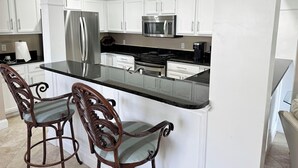 A modern kitchen with white cabinets, stainless steel appliances, and a central island with bar stools. - Beautiful Villa with Loft - 6 Passenger Golf Cart Included (Miramar Beach)