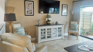 A living room with a beige sofa, a white cabinet, a flat-screen TV, and a window with curtains. - Beautiful Villa with Loft - 6 Passenger Golf Cart Included (Miramar Beach)