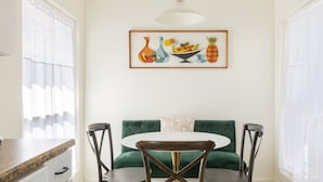 A dining area with a round table, two chairs, a green sofa, and a framed artwork above the table. - Downtown Napa!  Unit C Walk to Everything!  (Napa)