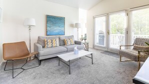 A living room with a grey sofa, a brown chair, a white coffee table, and a blue painting on the wall. - Downtown Napa!  Unit C Walk to Everything!  (Napa)