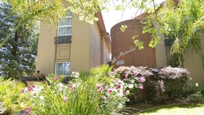 A building with a brick section and a beige facade, surrounded by lush greenery and flowering plants. - Downtown Napa!  Unit C Walk to Everything!  (Napa)