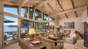 Amplia sala de estar con grandes ventanales con vistas a un lago, amueblada con un sofá, sillas y una mesa de comedor.