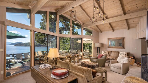 A spacious living room with large windows overlooking a lake, furnished with a sofa, chairs, and a dining table. - McCown Lakefront by Hauserman Rentals (Tahoma)