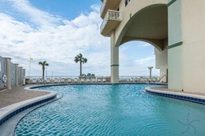 A swimming pool with a curved edge, a palm tree, and a building with a balcony.