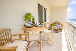 Une table en bois avec des chaises sur un balcon, un saladier rempli de fruits et une vue sur l’océan.