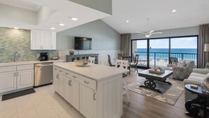 Eine geräumige Küche mit einer großen Kochinsel, ein Essbereich mit Meerblick und ein Wohnzimmer mit Sofa und Couchtisch.