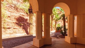 An arched corridor with stone columns, a gravel path, and a view of a desert landscape with palm trees. - The Skyline Villa - Family Getaway Heaven in the Heart of Saint George, UT (St George)