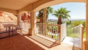 A covered outdoor area with a picnic table, white railing, and a view of palm trees and distant landscape. - The Skyline Villa - Family Getaway Heaven in the Heart of Saint George, UT (St George)