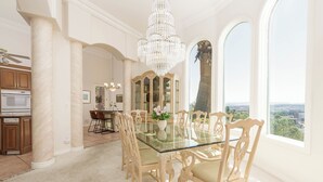 A dining room with a glass table, ornate chairs, a chandelier, and a view of the city through large windows. - The Skyline Villa - Family Getaway Heaven in the Heart of Saint George, UT (St George)