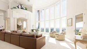 A spacious living room with a large brown sectional sofa, a small round table, and a view of the city through large windows. - The Skyline Villa - Family Getaway Heaven in the Heart of Saint George, UT (St George)