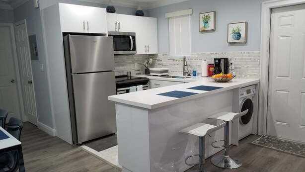 Una cocina moderna con electrodomésticos de acero inoxidable, una isla central con taburetes de bar y una lavadora integrada.