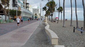 Un paseo marítimo con acera, palmeras y una playa al fondo.