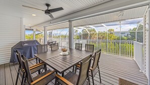 Eine überdachte Terrasse im Freien mit Tisch und Stühlen, einem Deckenventilator und Blick auf die umliegende Landschaft.