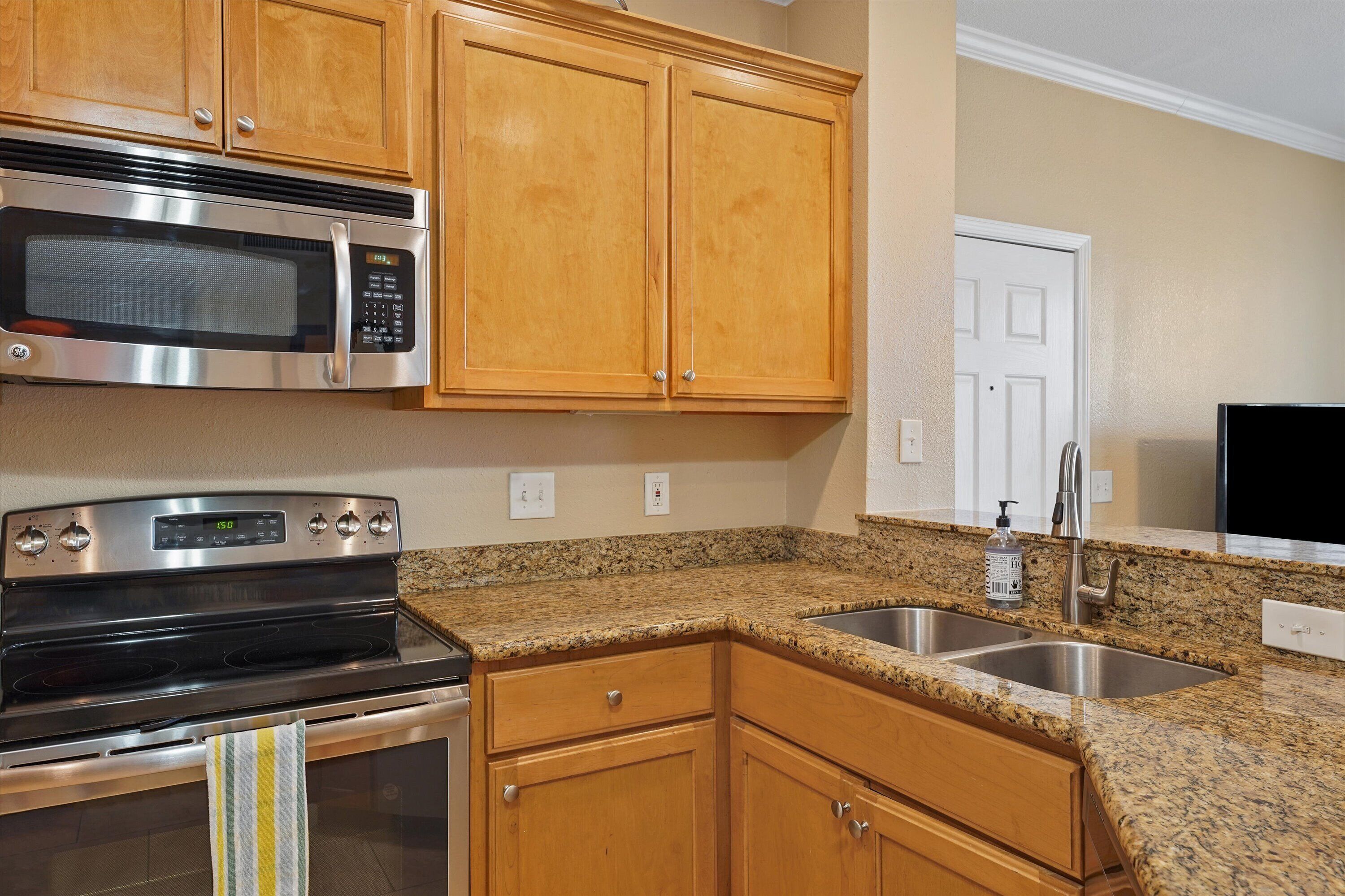 A kitchen with wooden cabinets, a stainless steel microwave, a stove, and a granite countertop.