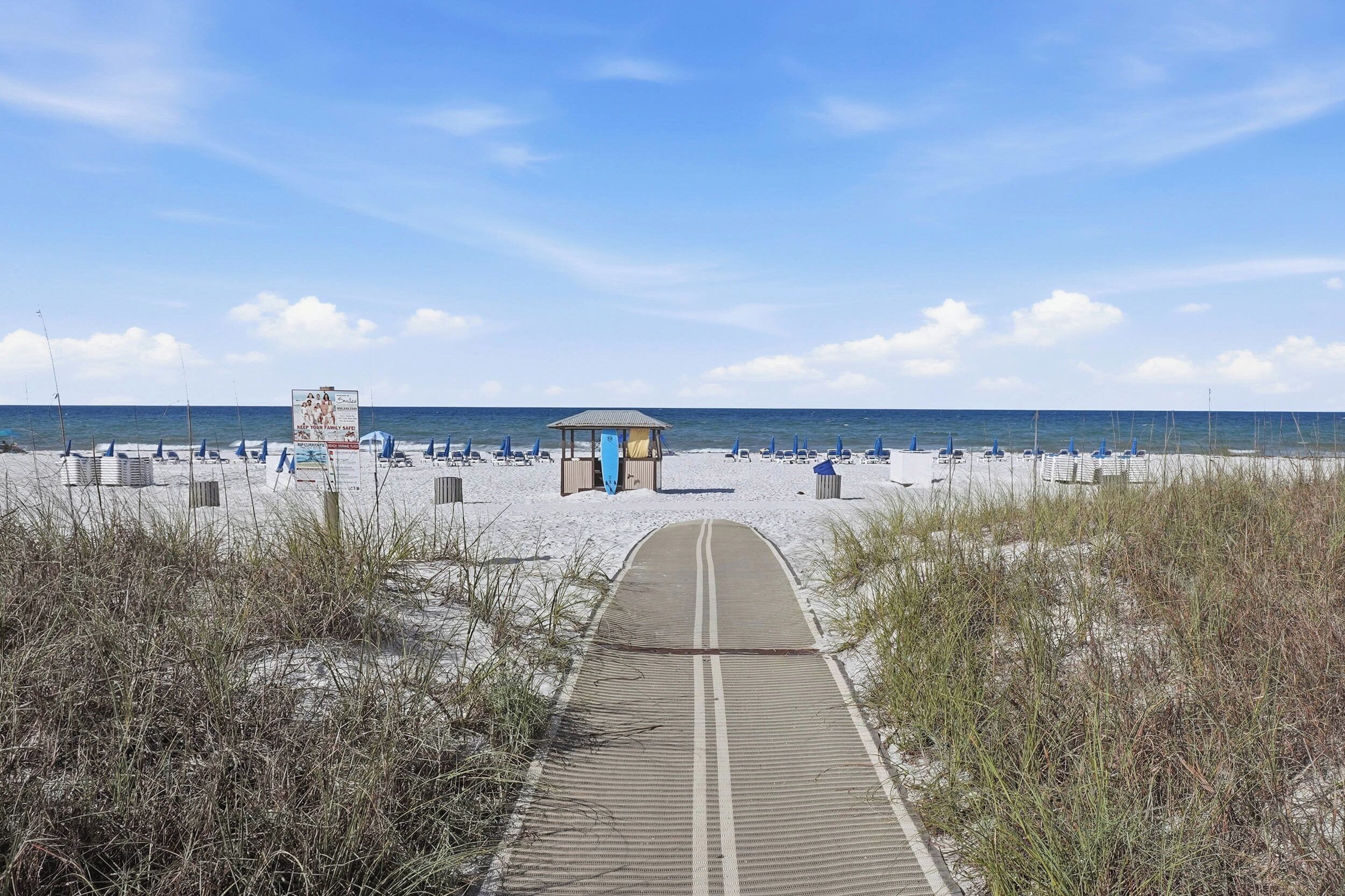 A beach pathway leading to a beach area with a small shelter and beach chairs.