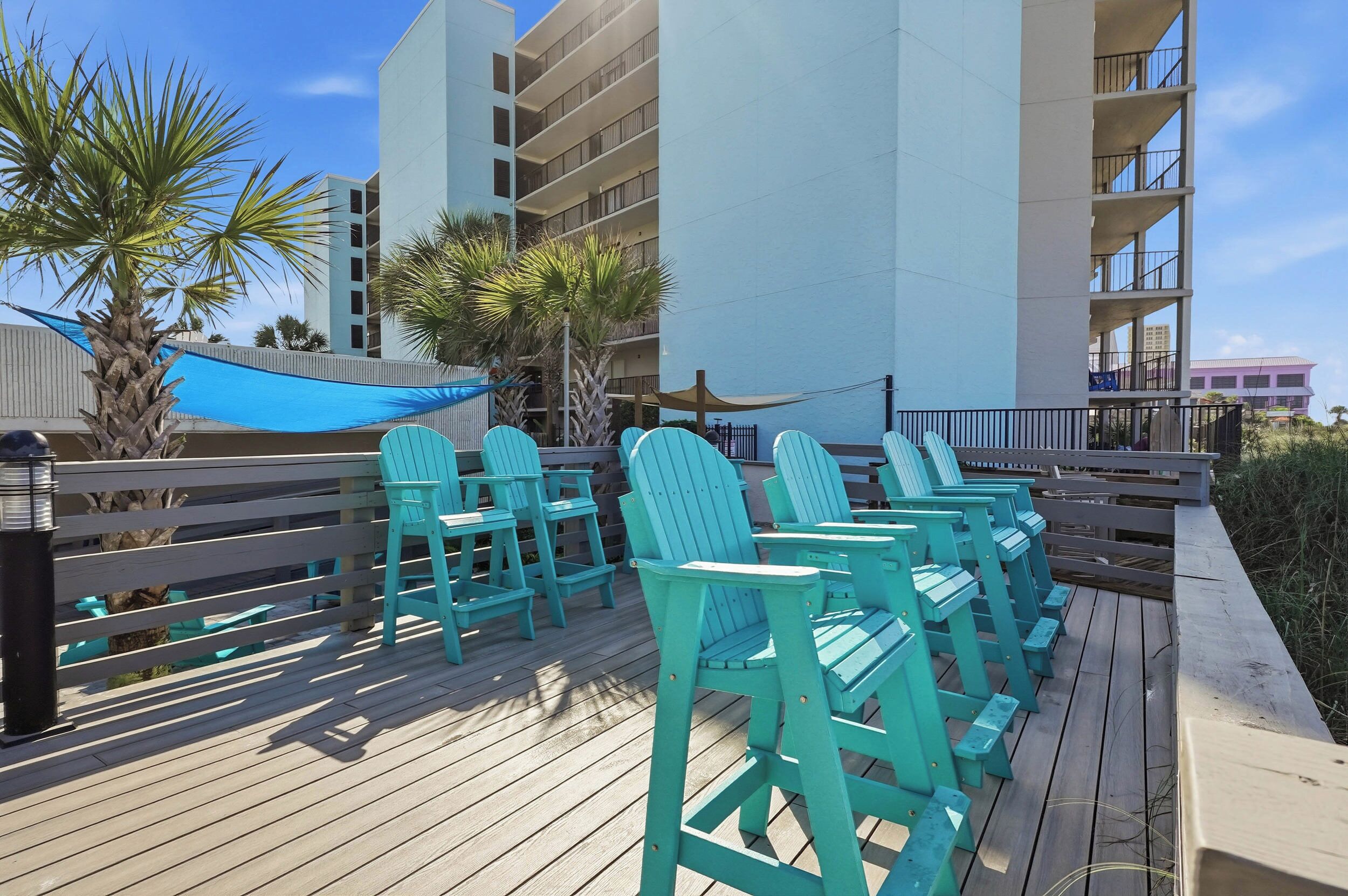 Une terrasse en bois avec des chaises turquoise et un auvent bleu.