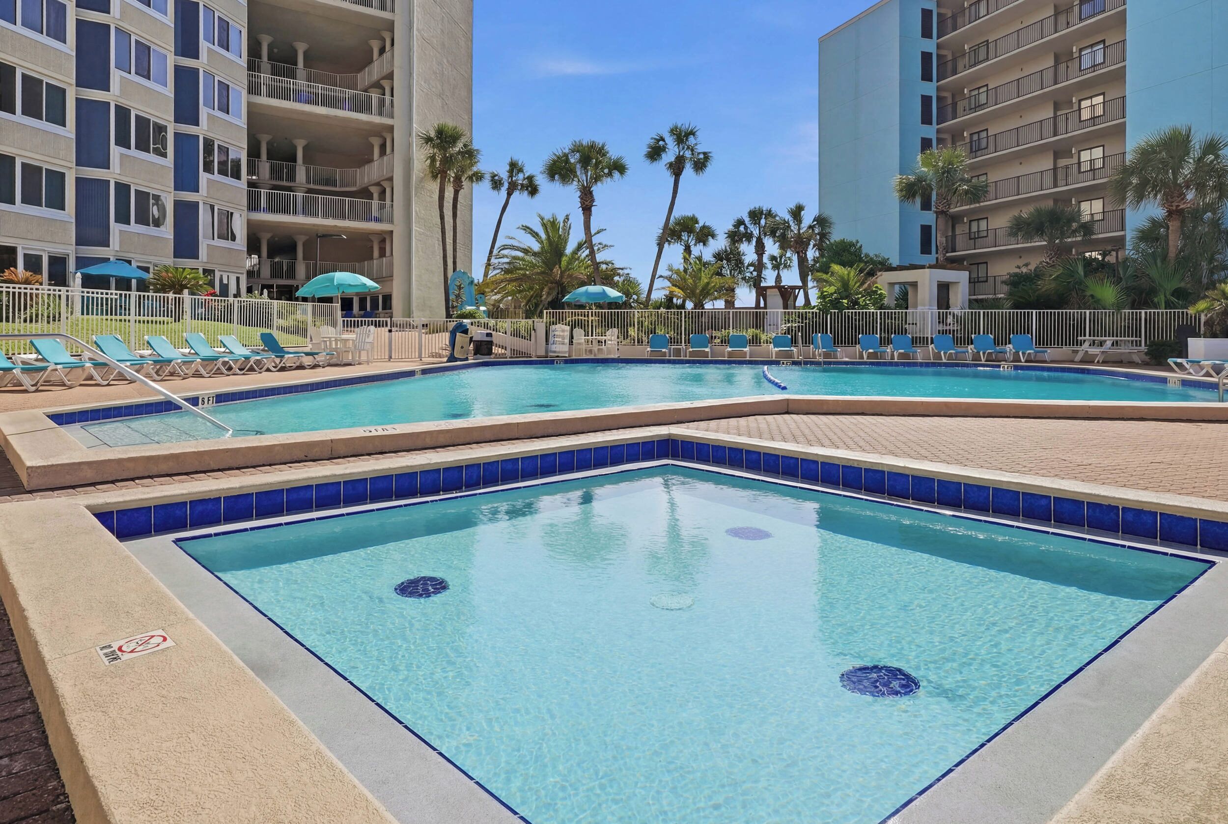 Uma área de piscina com várias piscinas, espreguiçadeiras e palmeiras.