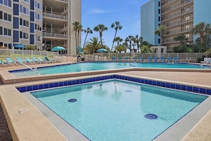 A pool area with multiple swimming pools, sun loungers, and palm trees.