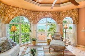 A spacious living room with a large window, a sofa, a coffee table, and a chair. - Sapphire blue water-white sandy beaches just steps from your front door-Luxury (Captiva)