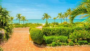 Ein gepflasterter Weg führt zu einem Strand mit Palmen und blauem Himmel.