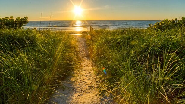 Ein Weg zum Strand, während die Sonne über dem Meer untergeht.