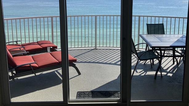 A balcony with red lounge chairs and a table, overlooking a clear blue sea. - OPEN 9/19-9/21 OR 9/26-10/1 GULF VIEW 12th floor Condo on the beach (Panama City Beach)