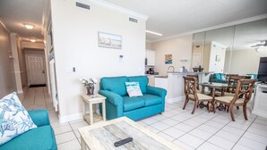 A living room with a teal sofa, a coffee table, and a dining area with wooden chairs and a table. - OPEN 9/19-9/21 OR 9/26-10/1 GULF VIEW 12th floor Condo on the beach (Panama City Beach)