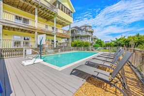 A pool area with a wooden deck, lounge chairs, and a basketball hoop. - Semi-Oceanfront Home w/ Pool, Hot Tub, Elevator, Cabana w/ Tiki Bar, Game Room (Salvo)