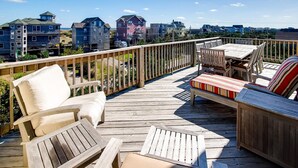 A wooden deck with outdoor furniture, including chairs and a sofa, overlooking a residential area with multiple houses. - Semi-Oceanfront Home w/ Pool, Hot Tub, Elevator, Cabana w/ Tiki Bar, Game Room (Salvo)