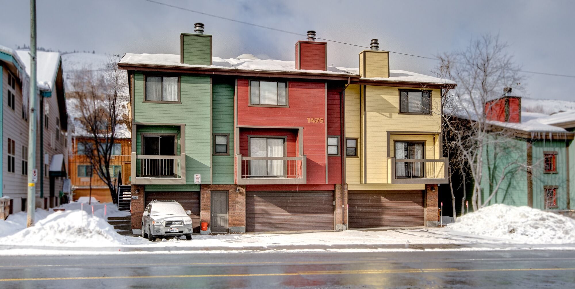 En flervåningsbostadsbyggnad med ett garage, en parkerad bil framför och snö på marken.