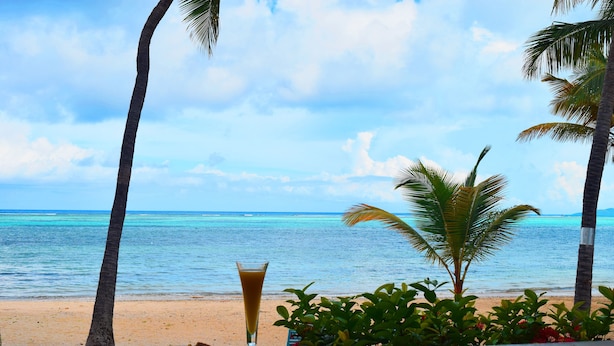 Uitzicht op een tropisch strand met een heldere lucht, palmbomen en een glas sinaasappelsap op een tafel.