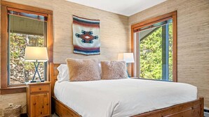 A bedroom with a wooden bed, two bedside tables, a lamp, a wall tapestry, and large windows. - RMR: Rendezvous A5 Condo in Teton Village (Teton Village)