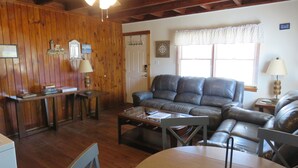 Una sala de estar acogedora con techo de madera, un sofá de cuero, una mesa de centro y una mesa de comedor.