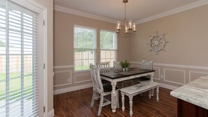 A dining room with a wooden table, white chairs, a chandelier, and a ship's wheel decoration. - Walk just 2 blocks to the beach! (PANAMA CITY BEACH)