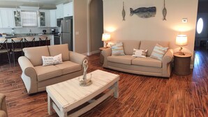 A living room with two sofas, a coffee table, and a kitchen in the background. - Walk just 2 blocks to the beach! (PANAMA CITY BEACH)