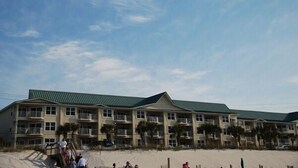 Un hotel a più piani con tetto verde e balconi, situato su una spiaggia sabbiosa.