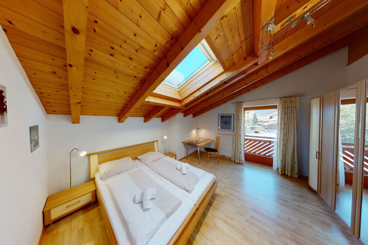 Een slaapkamer met een houten plafond, dakraam, bed, bureau en uitzicht.