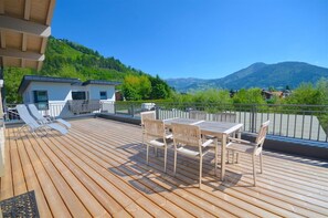 Une terrasse en bois avec une table et des chaises, offrant une vue sur un paysage montagneux.