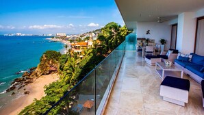 Un balcon offrant une vue dégagée sur l’océan et la plage, aménagé avec un canapé et des fauteuils.