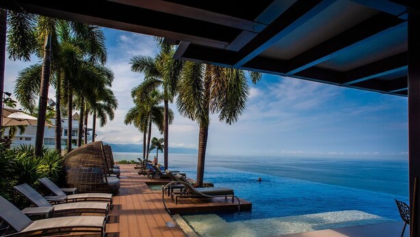 Un espace aménagé au bord de la piscine, avec des chaises longues et des palmiers, offrant une vue sur l’océan.