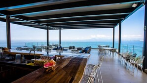 Un espace extérieur moderne, aménagé avec une table en bois et des chaises blanches, offrant une vue imprenable sur l’océan.