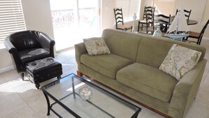 A living room with a green sofa, a black leather armchair, and a glass coffee table.